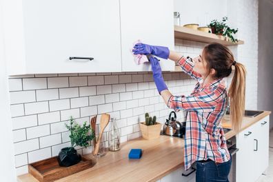 Woman in gloves cleaning cabinet with rag at home kitchen