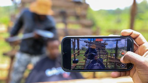 A man uses his phone to record barber and content creator Safari Martins as he shaves Ian Njenga in Kiambu, Kenya, Wednesday, Nov. 26, 2025. (AP Photo/Andrew Kasuku)