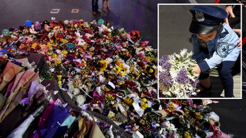 Floral tributes at the scene, and a child dressed in a police costume lays a bouquet. (AAP)