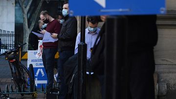 People wearing face masks wait in a queue at a COVID-19 testing site located at the Sydney Eye Hospital. 