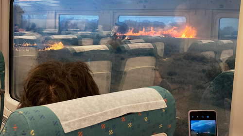 Passengers take photos at a wildfire while traveling on a train in Zamora, Spain, Monday, July 18, 2022. 