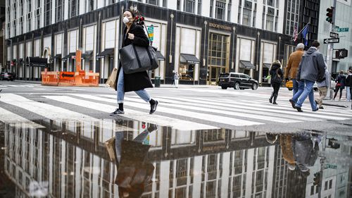 A pedestrian wearing a protective face mask is reflected in a rain puddle, Tuesday, March 17, 2020, in New York. New York state entered a new phase in the coronavirus pandemic this week.
