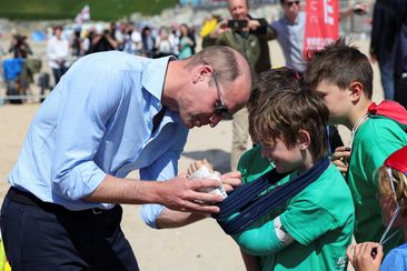 Prince William, the Duke of Cornwall, signs the cast of Felix Kanes, a member of Hollywell Bay Surf Life Saving Club, during a visit to Fistral Beach on May 9, 2024 in Newquay, Cornwall.