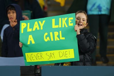 A fan of Australia, holding a sign which reads "Play Like A Girl Never Say Die!" , poses for a photograph as they enjoy the pre-match atmosphere prior to the FIFA Women's World Cup Australia & New Zealand 2023 Semi Final match between Australia and England at Stadium Australia.