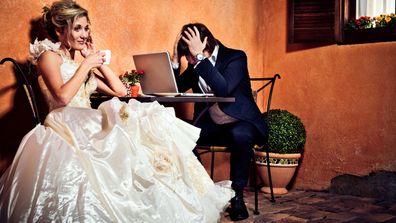 Stock image bride in wedding dress next to stressed out groom in front of computer