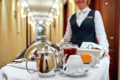Waitress in uniform delivering tray with food in a room of hotel. Room service. Selective focus on tableware. Horizontal shot