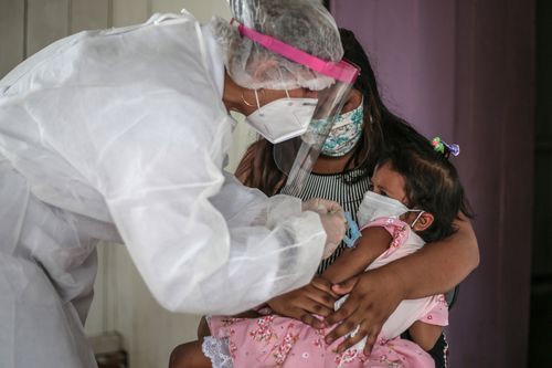 A mother holds her daughter while a nurse conducts an examination.