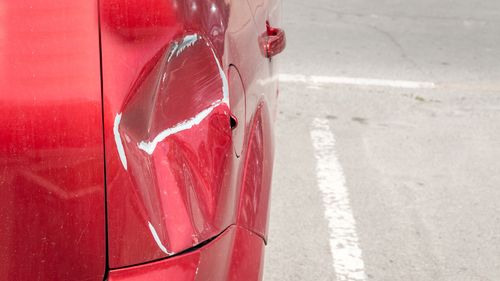 Red scratched car with damaged paint in crash accident or parking lot and dented damage of metal body from collision