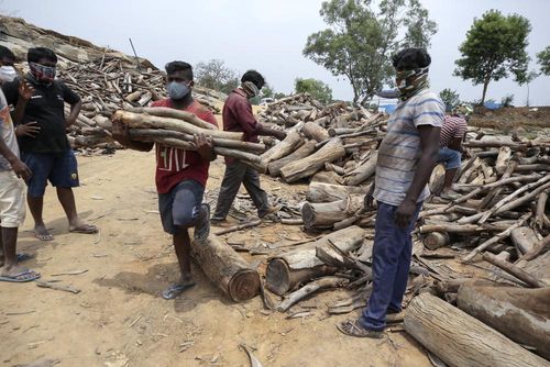 People carry wood as those who died of COVID-19 are cremated at an open crematorium on the outskirts of Bengaluru, Karnataka state, India.