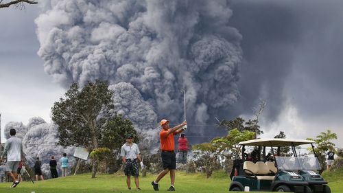 People play golf as an ash plume rises in the distance from the Kilauea volcano on Hawaii's Big Island on May 15, 2018 in Hawaii Volcanoes National Park, Hawaii. (Getty)