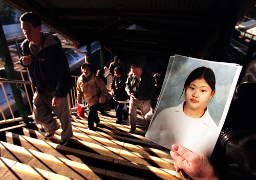 Photo taken in 1998 shows a man holding a search poster for missing schoolgirl Quanne Diec, as commuters in a Sydney train station walk up the stairs.