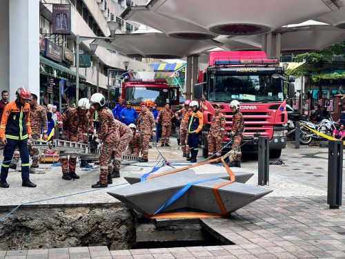 This photo provided by the Malaysia Fire and Rescue Department shows rescue personnel entering a deep sinkhole after receiving reports that a woman fell into the sinkhole after a section of the pavement collapsed in Kuala Lumpur, Friday, Aug. 23, 2024. 