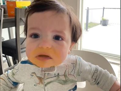 Baby sitting in high chair with a ring of orange stained around his mouth.