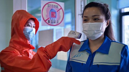 A health worker at the Pyongyang Cosmetics Factory takes the temperature of a woman arriving for her shift.