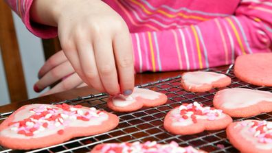 A young girl adds heart sprinkles to her Valentine's cookies.  Don't they look delicious?