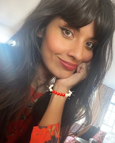 Jameela Jamil in red and black, smiling at the camera
