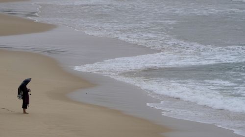 A woman stands under her umbrella as she watches large swells at Bondi Beach in Sydney.