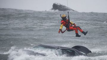 A US Coast Guard diver is lowered from a hovering helicopter to pull a body from a submerged vehicle stuck in rushing rapids just metres from the edge of Niagara Falls.