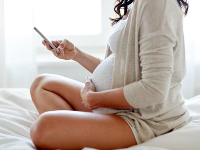 pregnancy, motherhood, technology, people and expectation concept - close up of pregnant woman with smartphone in bed at home