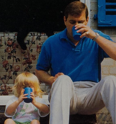 Princess Eugenie as a toddler sitting next to her father drinking out of matching blue cups.