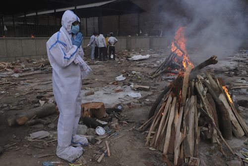 A man wearing personal protective equipment prays in front of the burning funeral pyre of his father who died of COVID-19, at a crematorium in New Delhi, India, Tuesday, May 11, 2021. 