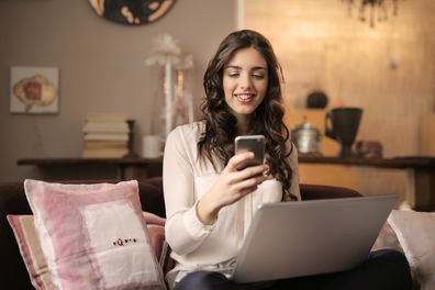 Woman sitting on a lounge using a phone and laptop