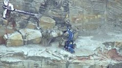 Emergency staff have reached the rock ledge where the man fell from a cliff. (9NEWS)