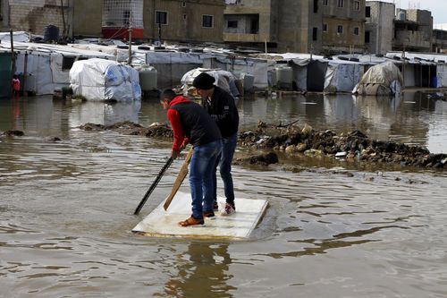 Syrian refugees use a floating piece of wood to move around after heavy rain.