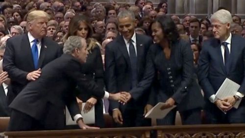 George W Bush hands a small item to Michelle Obama before the funeral for his father, George HW Bush.