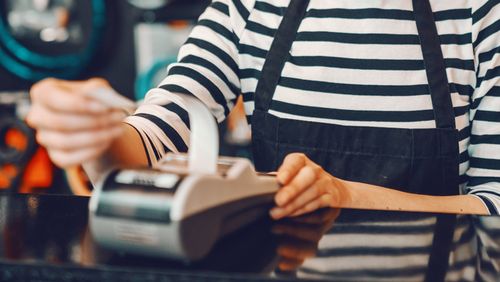 Trabalhadora caucasiana sorridente com cabelo loiro curto e óculos usando caixa registradora em pé na loja de bicicletas.