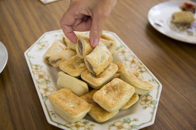 Australian snack, party pies and sausage-rolls on a plate with fingers selecting one.