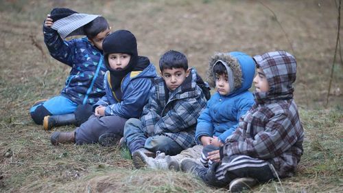 Migrant children sit on the ground as other migrants from the Middle East and elsewhere gather at the Belarus-Poland border.