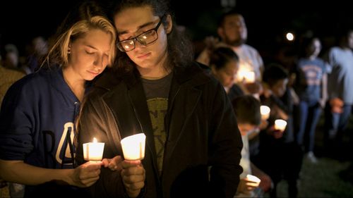 Bailey LeJeaune, 17, and David Betancourt, 18, hold candles during a vigil for the victims. (Image: AAP)