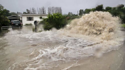 Water gushes from a storm drain access port on a street in Te Awanga, southeast of Auckland, New Zealand, Tuesday, Feb. 14, 2023.  