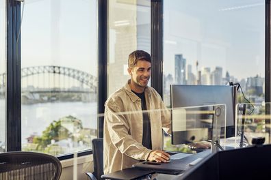 Single worker in an Australian office environment. Views of Sydney harbour and city skyline. Open plan office