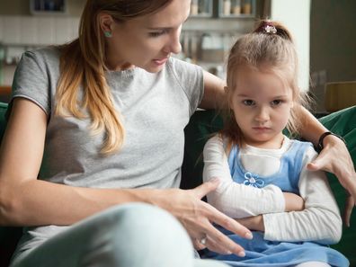 Angry offended little girl ignoring not listening mother words, advice, mum hugging, talking with stubborn, upset daughter at living room, bad upbringing, difficult behavior of child