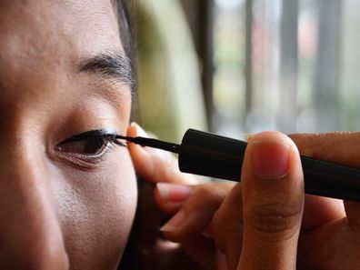 Woman applying liquid eyeliner to her eyes