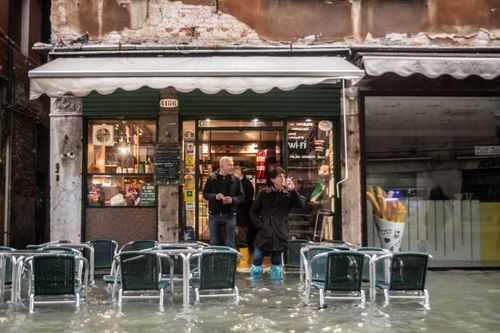 A cafe customer smokes a cigarette with boots covered in plastic to keep the water out.