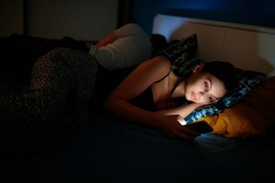Young woman sending text message as her boyfriend sleeps in the bed