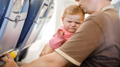 Young tired father and his crying baby daughter during flight on airplane going on vacations. 