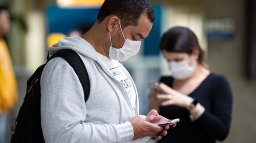 Passengers wearing masks as a precaution against the spread of the new coronavirus COVID-19 use their phones at the Sao Paulo International Airport in Sao Paulo, Brazil, Thursday, Feb. 27, 2020. (AP Photo/Andre Penner)