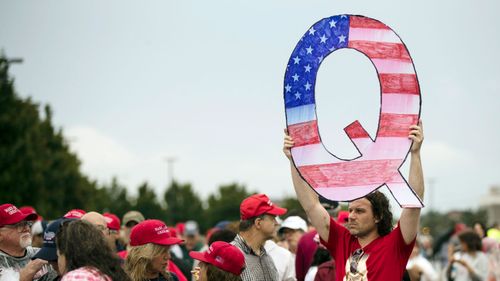 A protesters holds a Q sign waits in line with others to enter a campaign rally with President Donald Trump in August 2014.