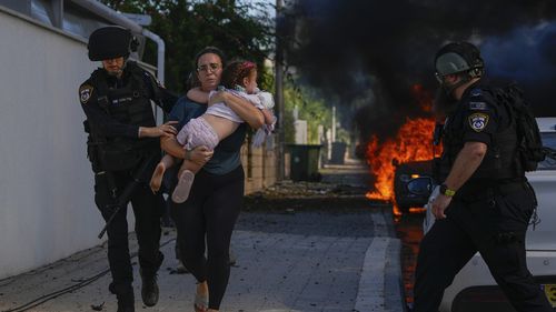 Police officers evacuate a woman and a child from a site hit by a rocket fired from the Gaza Strip, in Ashkelon, southern Israel, Saturday, Oct. 7, 2023.  