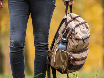 Female hiker holding backpack in hand. Woman trekking in autumn forest. Adventure in nature