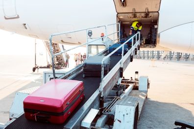 Exterior shot of a young man taking luggage off the plane. Airport ground crew at work.