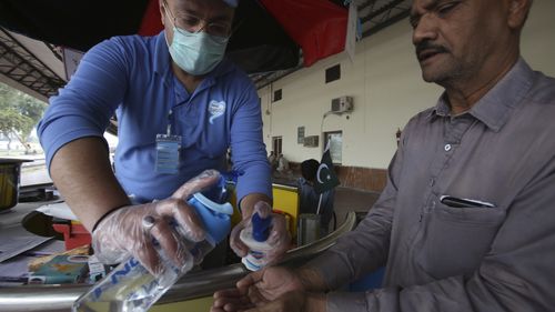 A Pakistani volunteer helps a passenger arriving at a railway station to wash hands as a measure to help prevent the spread of the coronavirus.