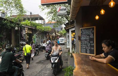 Ubud, Bali - February 12, 2017: Pedestrians and people on scooters move down a street lined with shops and restaurants in Ubud, Bali.