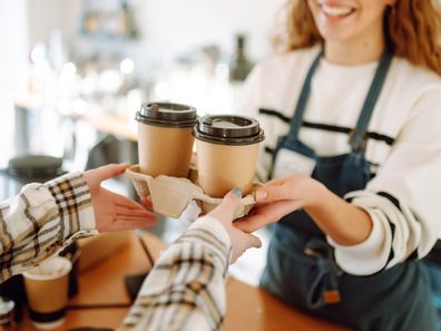 Smiling barista girl giving take away coffee cups to a customers.