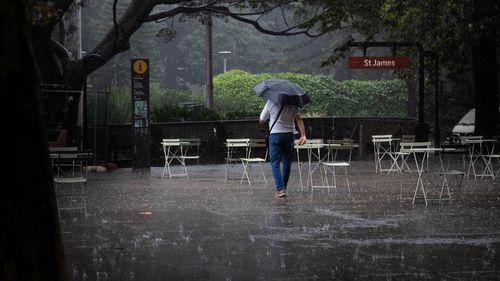 A pedestrian walks through a deserted outdoor cafe in heavy rainfall in Sydney's CBD.