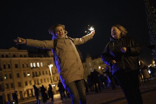 A woman holds a sparkler as she dances in Sophia Square before curfew on New Year's Eve in Kyiv, Ukraine, Saturday, Dec. 31, 2022. 
